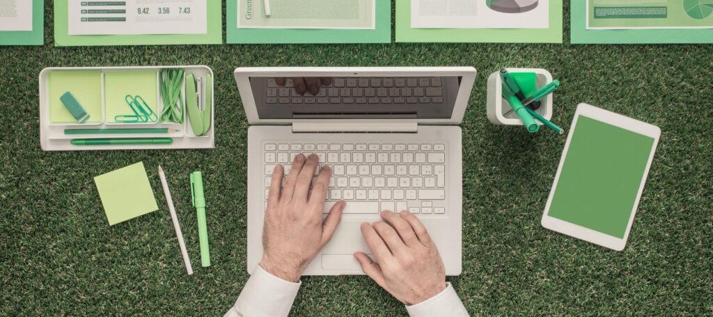 a top-down view of a person using a laptop on grass, with green stationary and devices, used for the web hosting blog