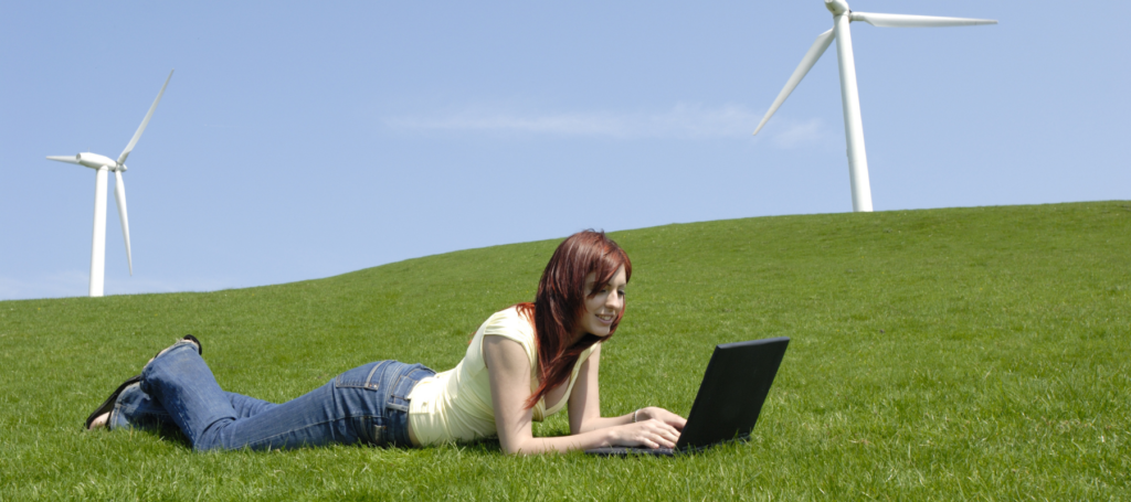 a woman laying in a green field with wind turbines, on her laptop. Used for the web hosting blog